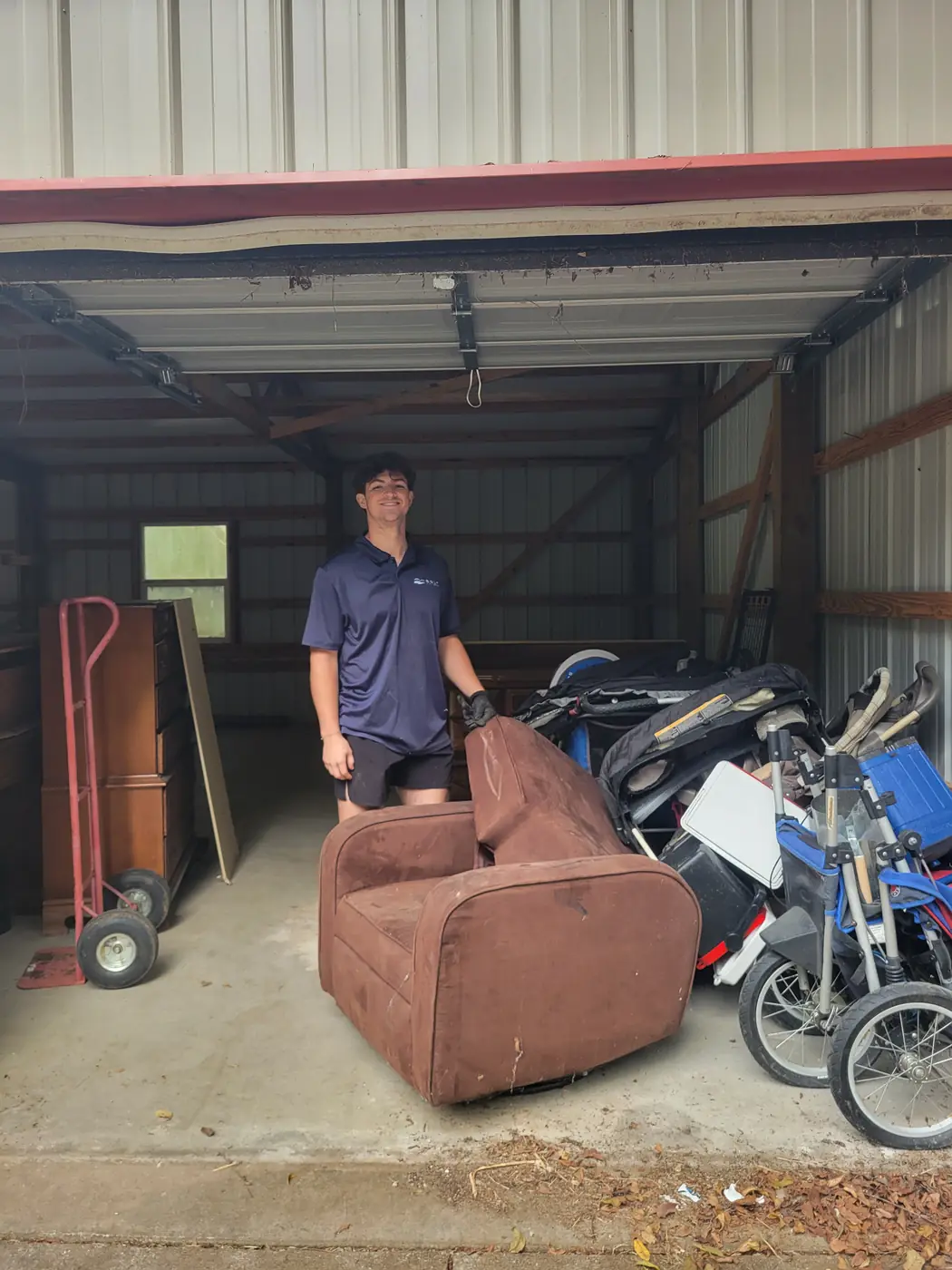 BoroBoys crew member hauling an old recliner, dresser and strollers out of a storage building