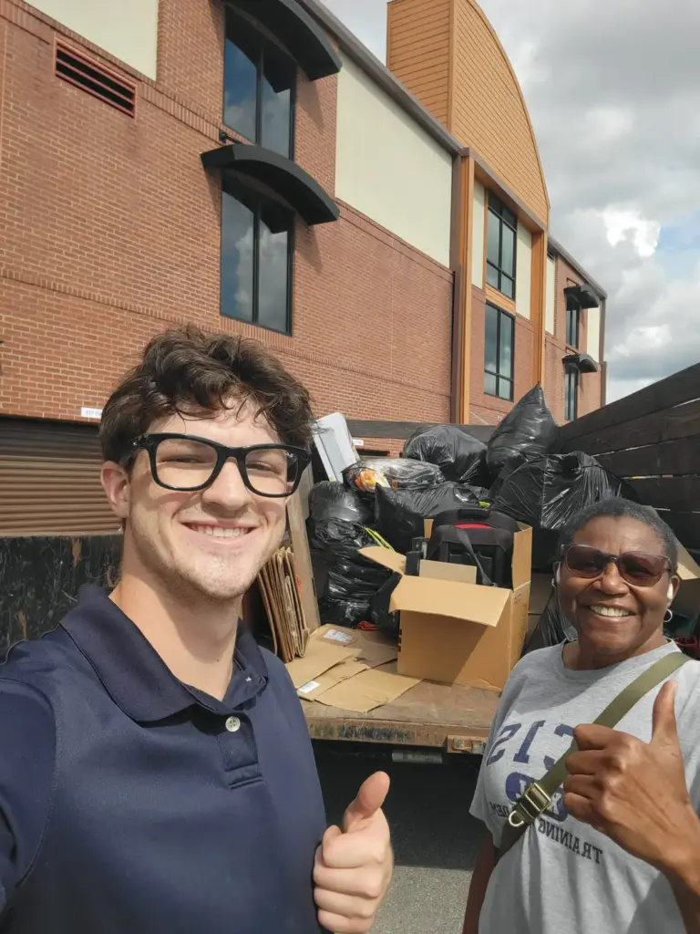 Satisfied customer with a BoroBoys crew member beside a trailer full of junk from a storage unit cleanout